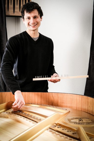 Ein Mann mit einem Holzstück, lächelnd, steht vor einem Möbelstück.